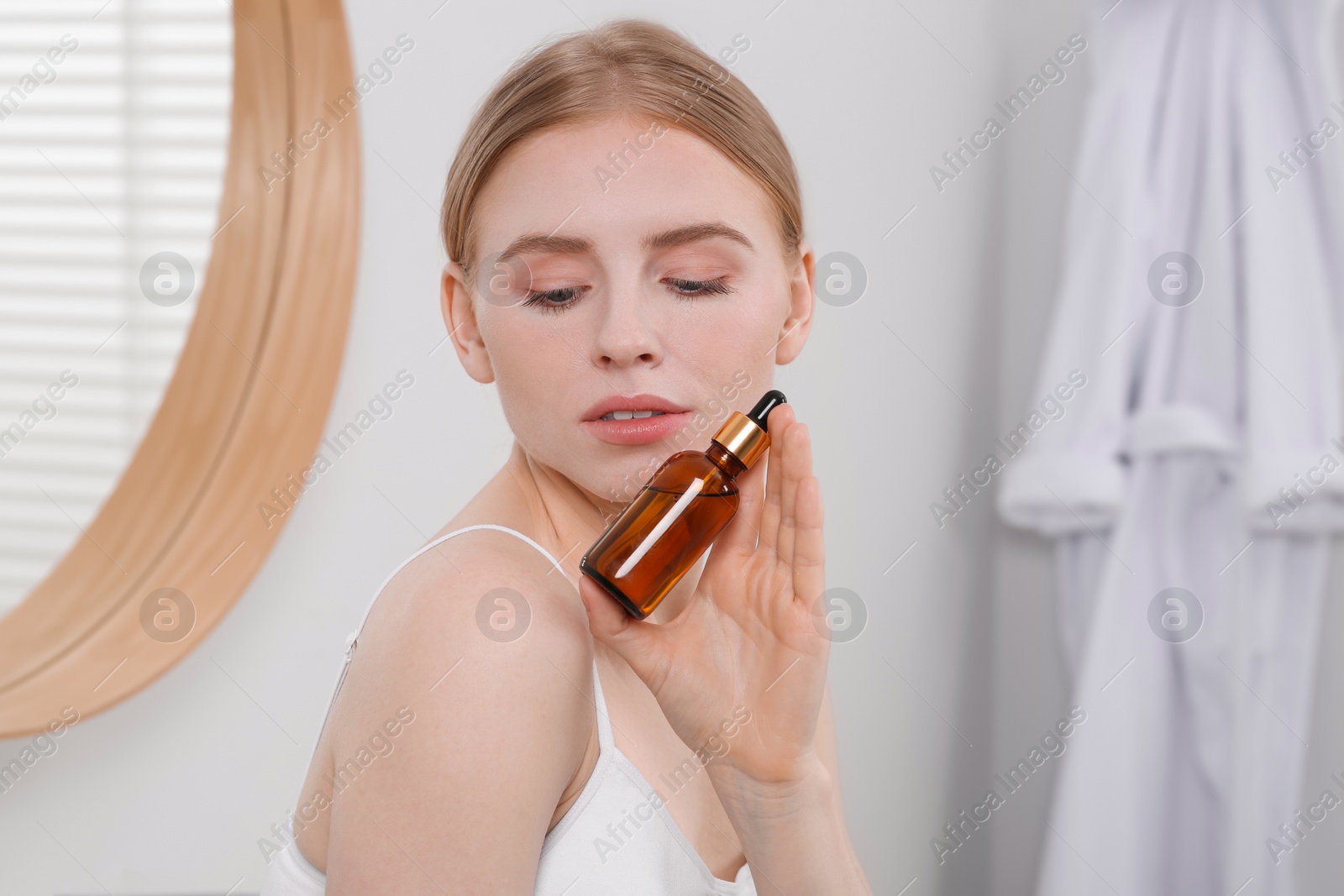 Photo of Young woman with bottle of essential oil in bathroom