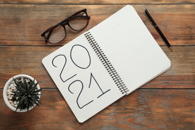 Photo of Notebook with number 2021, new year goals. Objects on wooden table, flat lay