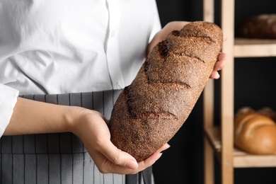 Baker holding loaf of bread indoors, closeup