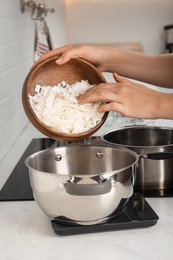 Photo of Woman pouring wax flakes into pot on scale in kitchen, closeup. Making homemade candles