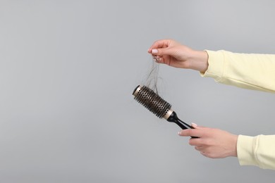 Photo of Woman untangling her lost hair from brush on grey background, closeup and space for text. Alopecia problem