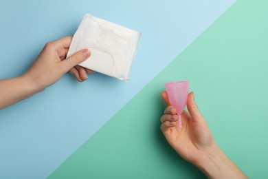 Photo of Women holding menstrual cup and pad on color background, top view
