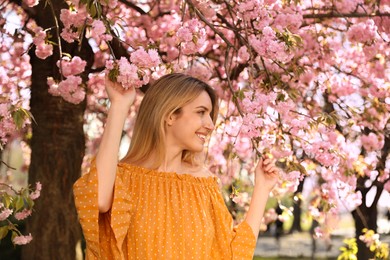 Photo of Young woman wearing stylish outfit near blossoming sakura in park. Fashionable spring look