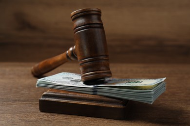 Photo of Law gavel with stack of dollars on wooden table, closeup