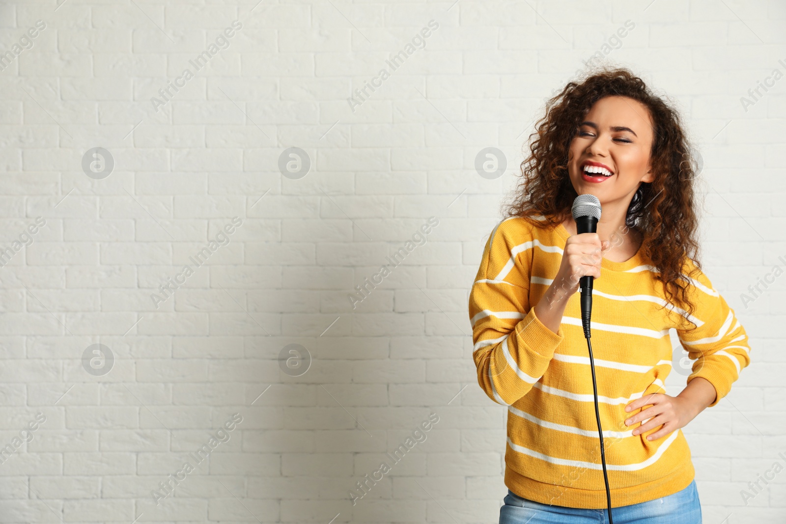 Photo of Portrait of curly African-American woman singing in microphone near brick wall. Space for text