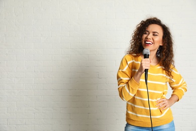 Photo of Portrait of curly African-American woman singing in microphone near brick wall. Space for text