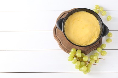 Photo of Fondue with tasty melted cheese and grapes on white wooden table, flat lay. Space for text