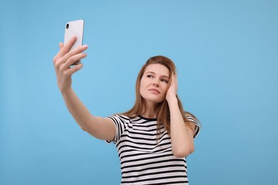 Beautiful woman taking selfie on light blue background