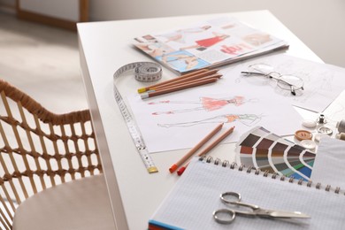 Sketches of clothes and different stuff on white table indoors. Fashion designer's workplace