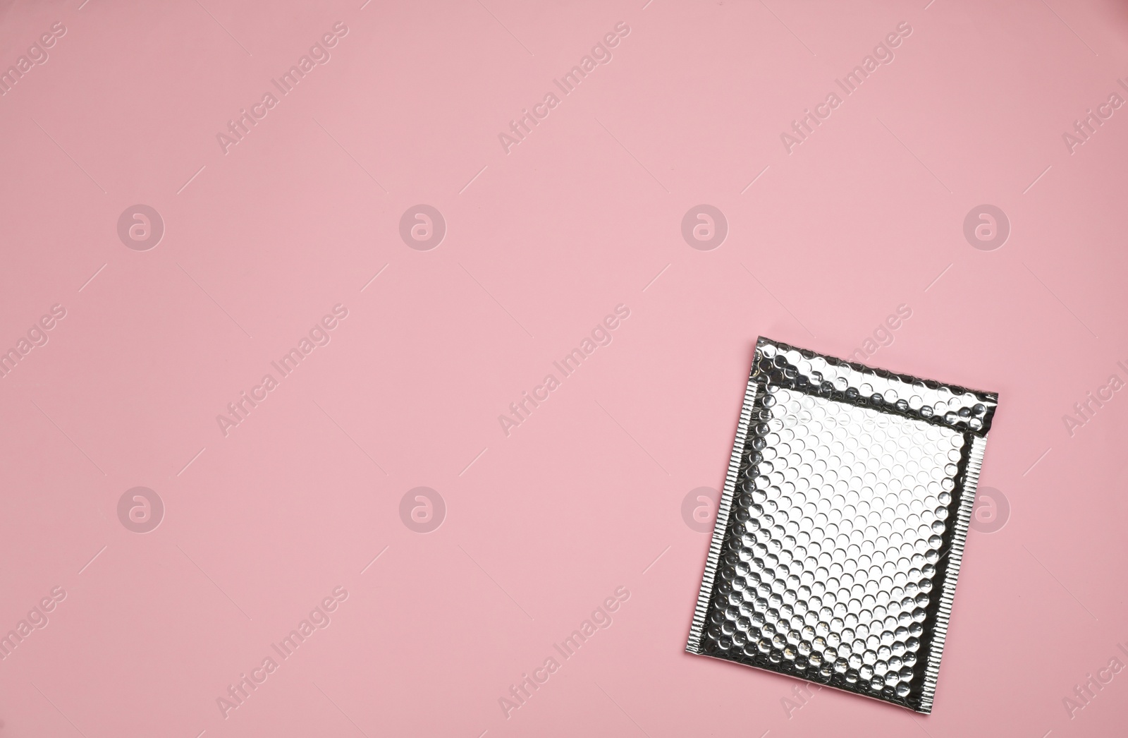 Photo of Padded envelope with bubble wrap on light pink background, top view. Space for text