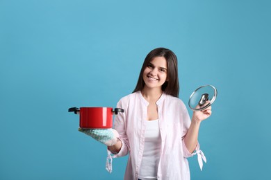 Photo of Happy young woman with cooking pot on light blue background