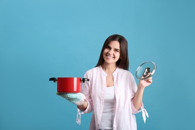 Happy young woman with cooking pot on light blue background