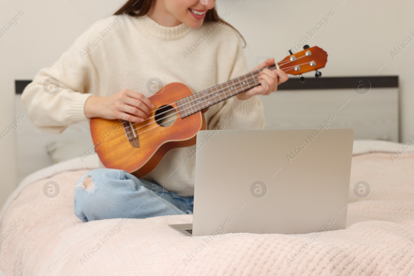 Photo of Woman playing ukulele while watching online music course via laptop at home, closeup. Time for hobby