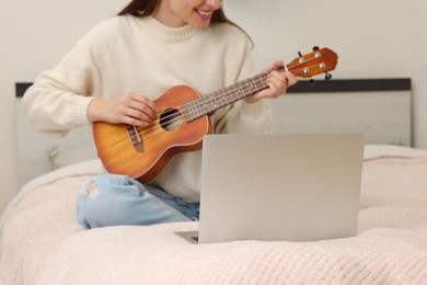 Photo of Woman playing ukulele while watching online music course via laptop at home, closeup. Time for hobby