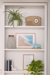 Photo of Interior design. Shelves with stylish accessories, potted plants and picture near white wall