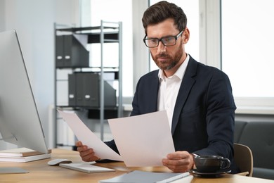 Photo of Handsome bearded man working with documents at table in office