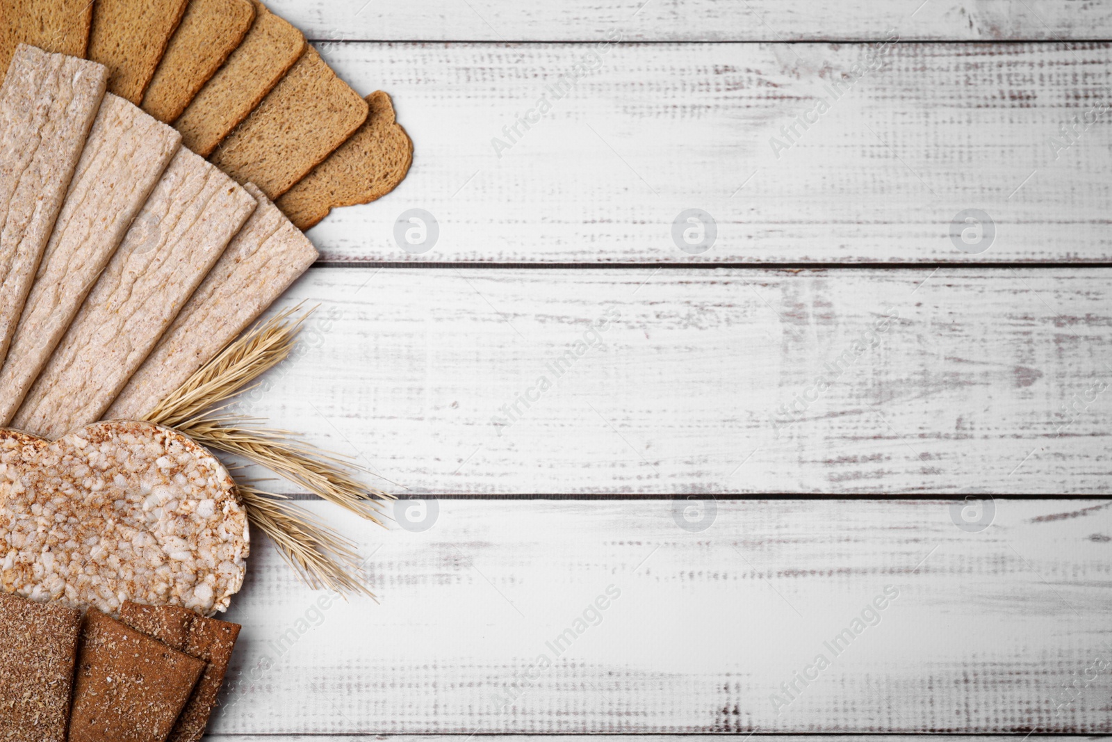 Photo of Rye crispbreads, rice cakes and rusks on white wooden table, flat lay