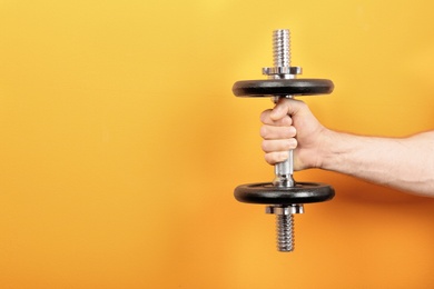 Photo of Male athlete holding metal dumbbell on color background. Space for text