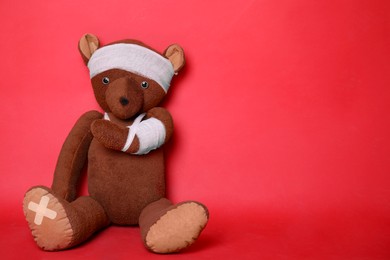 Photo of Toy bear with bandages on red background. Space for text