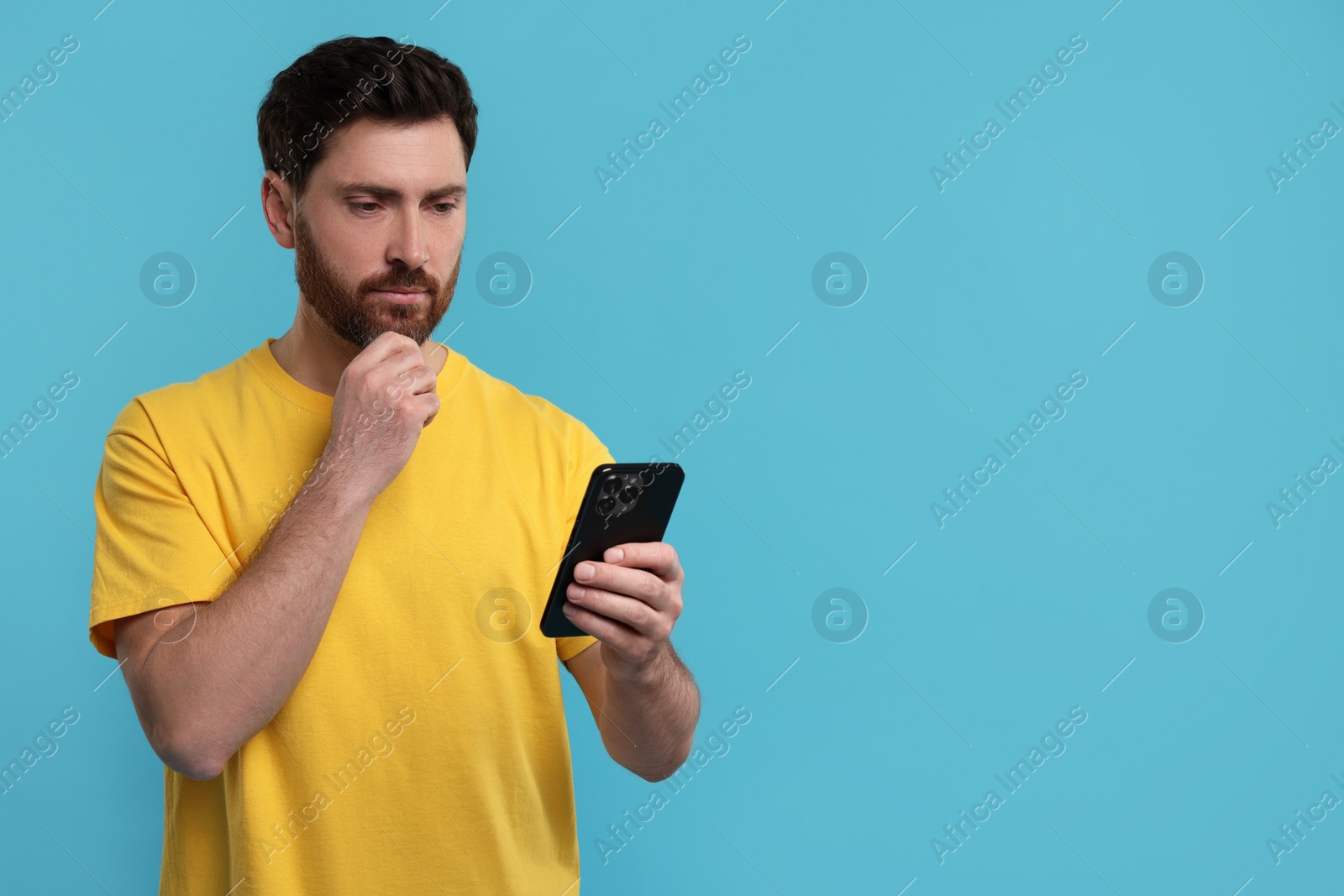 Photo of Handsome man using smartphone on light blue background. Space for text