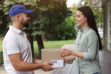 Photo of Woman receiving parcel from courier outdoors. Delivery service
