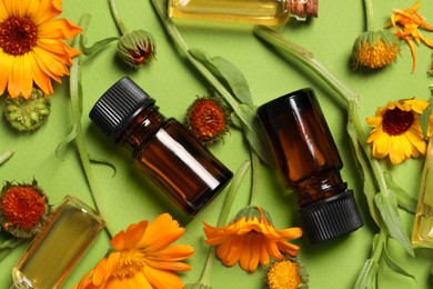 Bottles of essential oils and beautiful calendula flowers on green background, flat lay