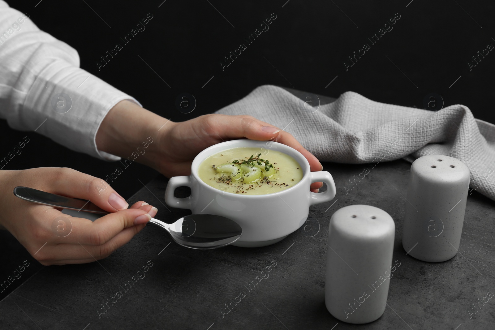 Photo of Woman with bowl of delicious celery soup at gray table, closeup