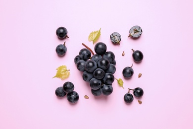 Photo of Bunch of ripe dark blue grapes with leaves on pink background, flat lay
