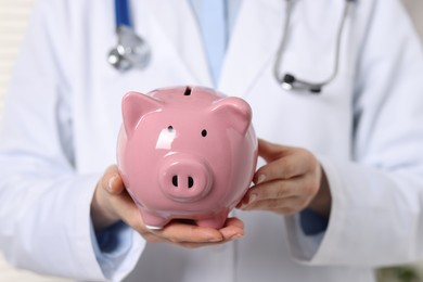 Photo of Doctor with pink ceramic piggy bank, closeup