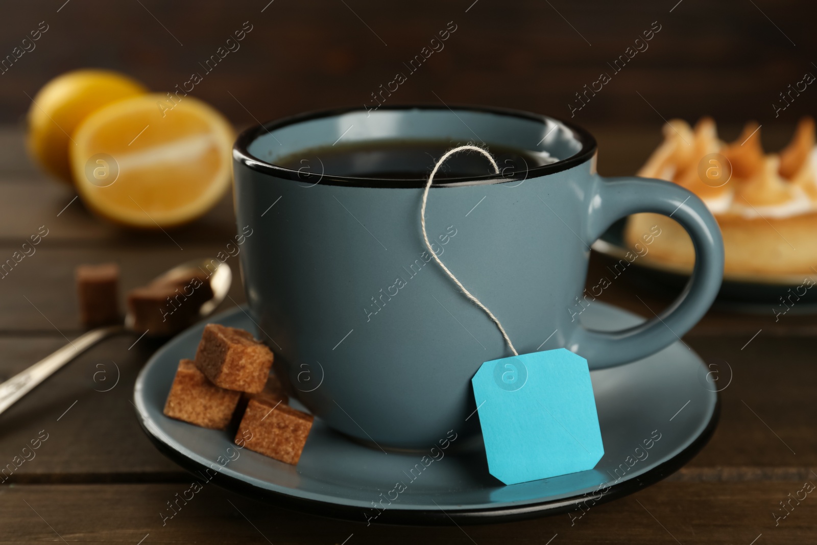 Photo of Tea bag in ceramic cup of hot water and sugar cubes 
on wooden table, closeup