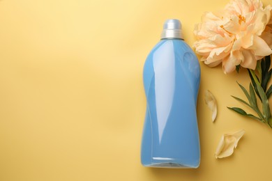 Photo of Bottle of fabric softener and beautiful peony flower on pale yellow background, flat lay. Space for text