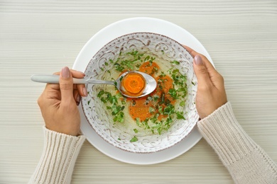 Photo of Woman with bowl of soup at wooden table, top view. Flu treatment