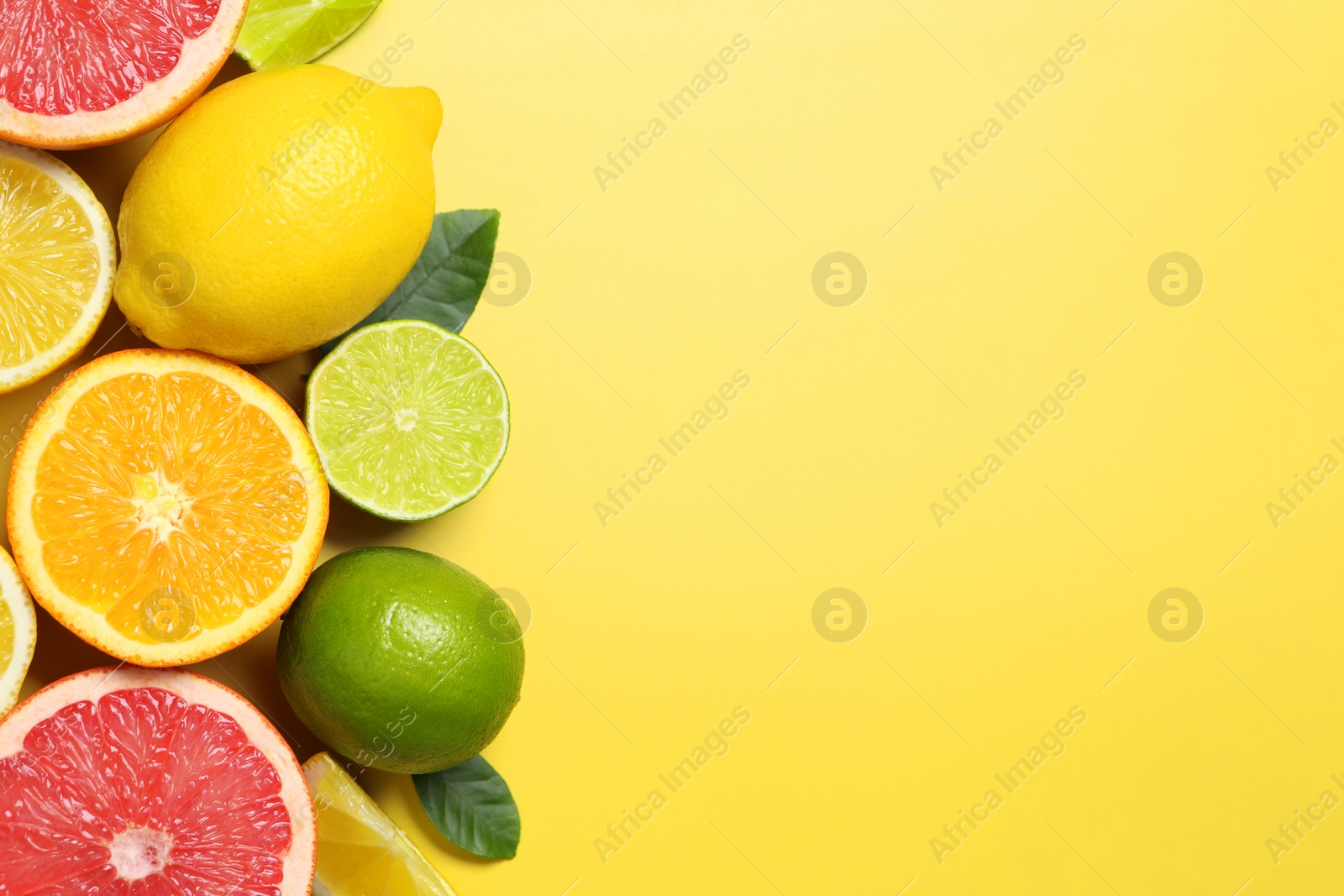 Photo of Different cut and whole citrus fruits on yellow table, flat lay. Space for text