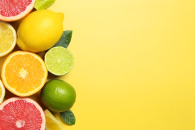 Photo of Different cut and whole citrus fruits on yellow table, flat lay. Space for text