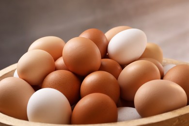 Photo of Fresh chicken eggs in bowl on light brown background, closeup