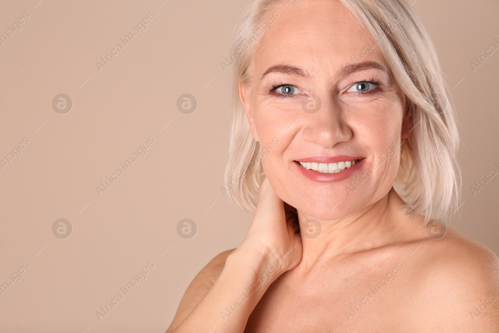 Photo of Portrait of charming mature woman with healthy beautiful face skin and natural makeup on beige background, closeup. Space for text