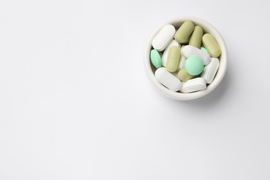 Photo of Different vitamin pills in bowl on white background, top view. Space for text