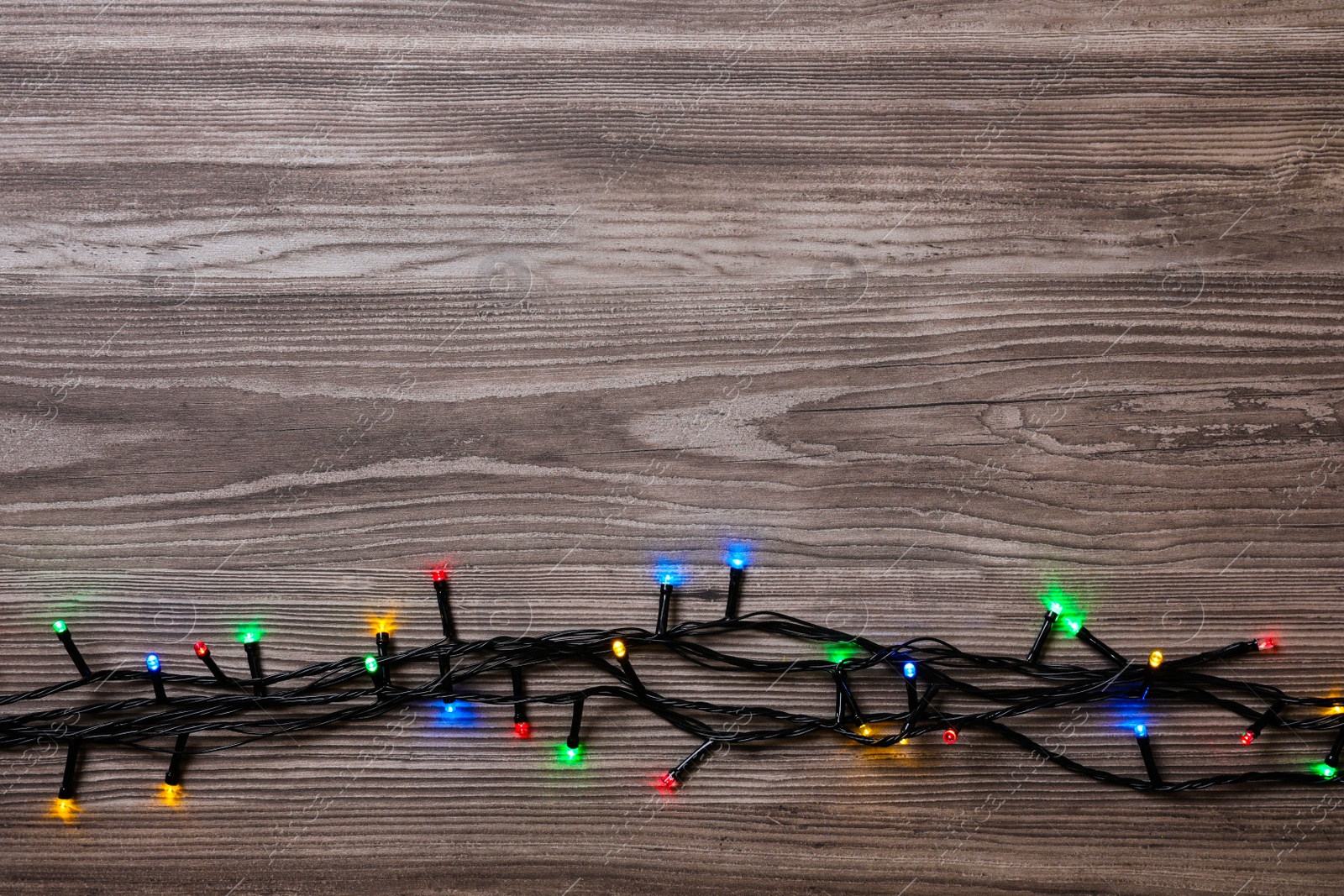 Photo of Christmas lights on wooden table, top view. Space for text