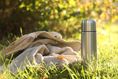 Metal thermos and bag with blanket on green grass outdoors