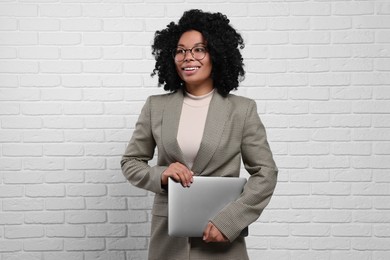 Young businesswoman holding laptop near white brick wall