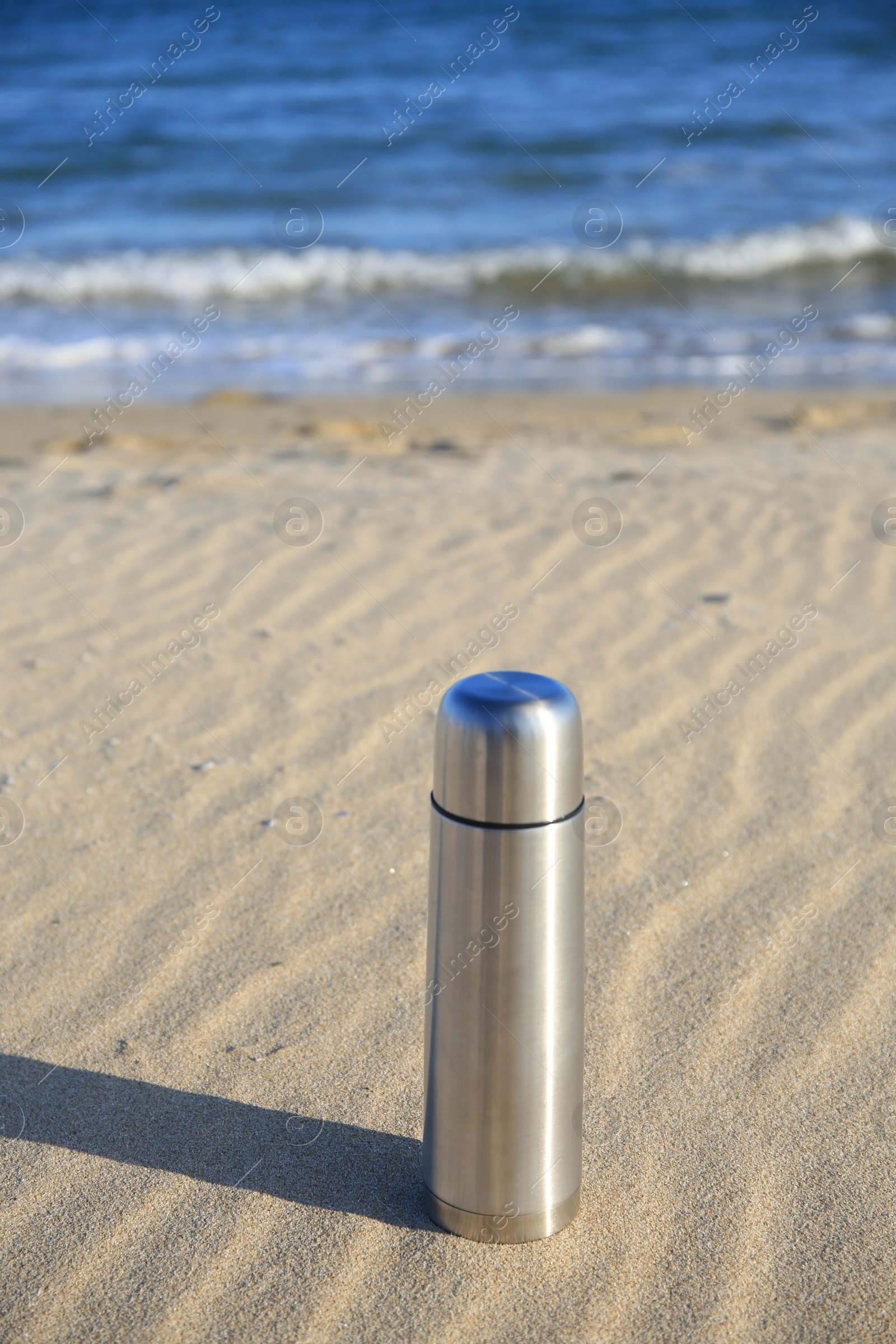 Photo of Metallic thermos with hot drink on sand near sea