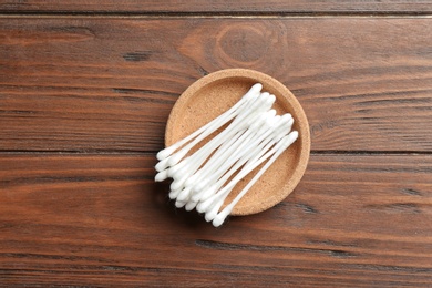 Plate with cotton swabs on wooden background, top view