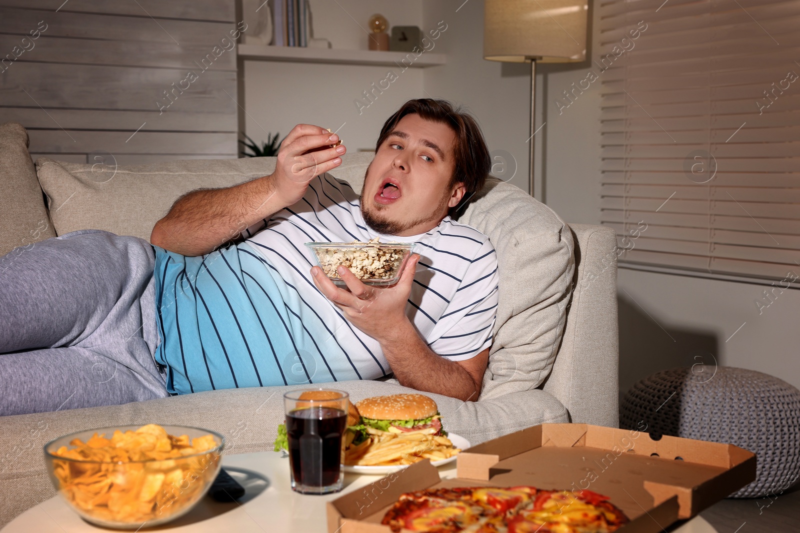 Photo of Overweight man with bowl of popcorn on sofa at home