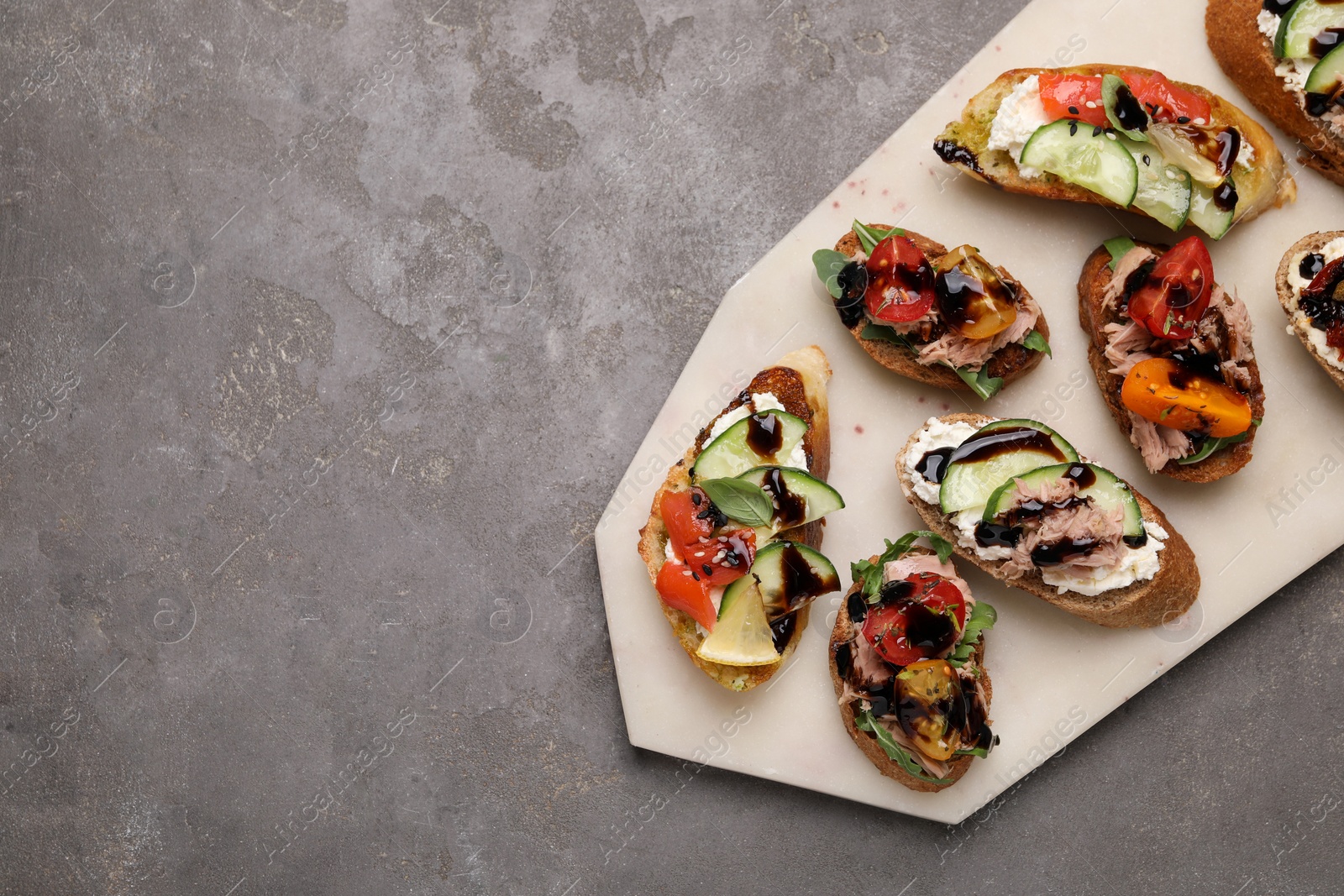 Photo of Delicious bruschettas with balsamic vinegar and different toppings on grey textured table, top view. Space for text