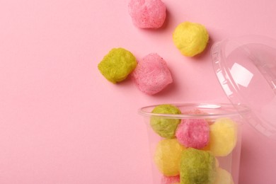 Plastic cup with color cotton balls on pink background, flat lay and space for text. Sweet candy