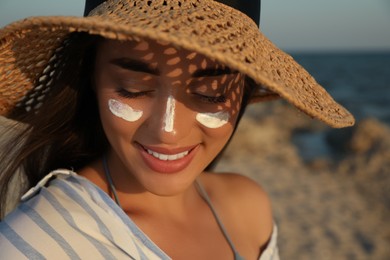 Photo of Happy young woman with sun protection cream on face at beach