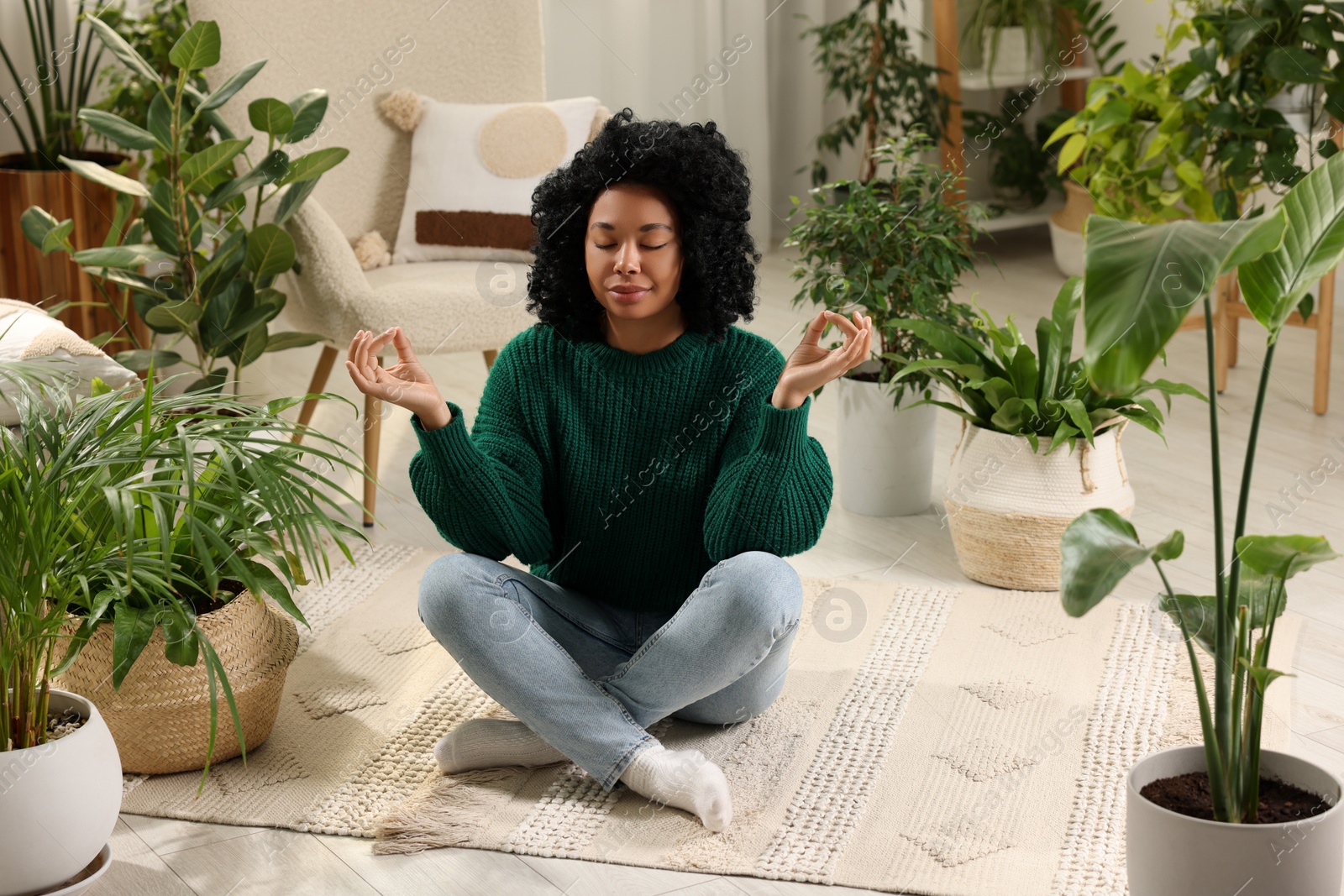 Photo of Relaxing atmosphere. Woman meditating near potted houseplants in room