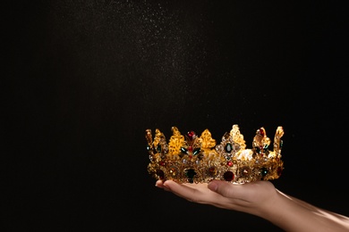 Photo of Woman holding beautiful golden crown on black background, closeup with space for text. Fantasy item