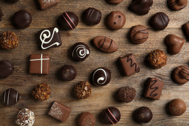 Photo of Different delicious chocolate candies on wooden table, flat lay