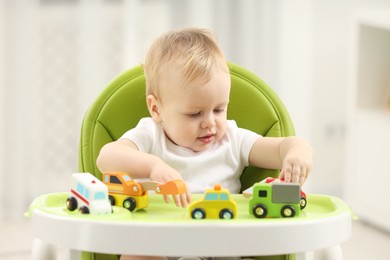 Children toys. Cute little boy playing with toy cars in high chair at home